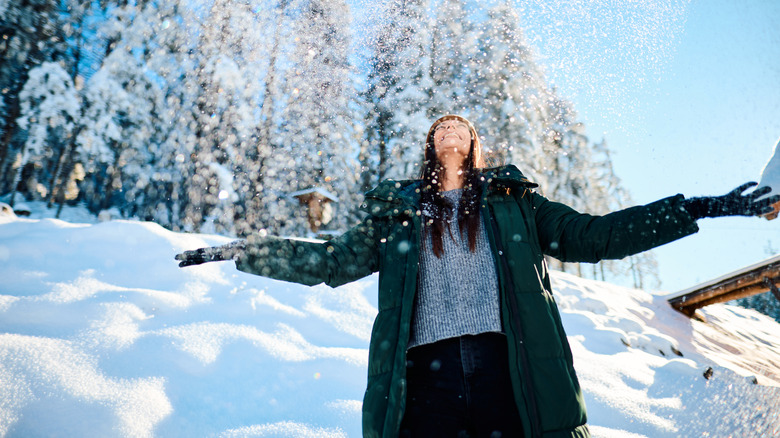 A young woman joyfully throwing snow into the air while enjoying the beauty of a winter forest.