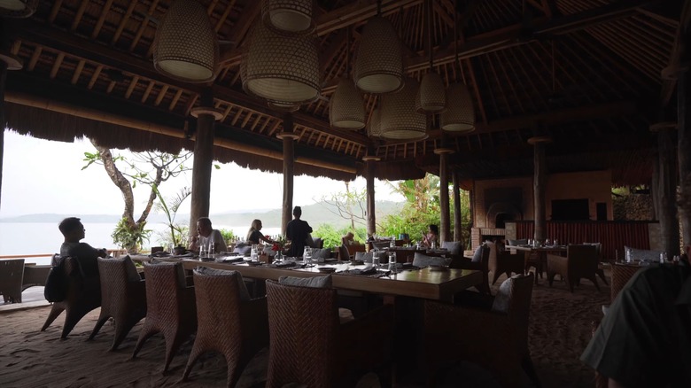 Patrons sit at tables in an open-air resort restaurant overlooking misty water