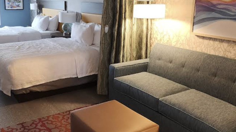 Interior view of studio-style suite at Home2 Suites by Hilton Santa Rosa Beach with curtain between two beds and living area with sofa, and soft task lighting