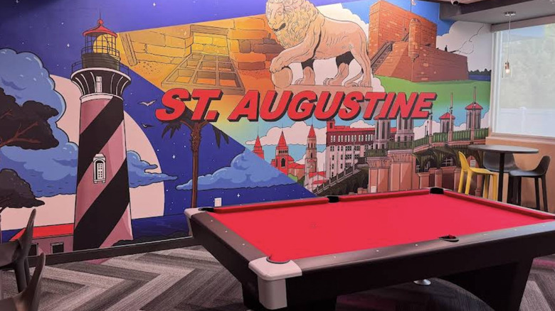 View of brightly colored "St. Augustine" mural featuring local landmarks behind a pool table in the lobby of Tru by Hilton St. Augustine I-95