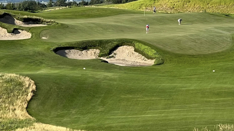 View of players on the green at Landmand Golf Club, Nebraska, with rolling hills on the fairway and bunkers on the lefthand side