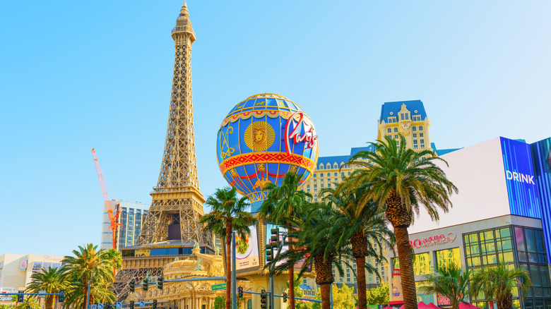 Daytime view of the Las Vegas Strip with palm trees in the foreground and Paris Las Vegas Eiffel Tower replica and hot air balloon in the background