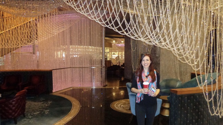 Woman wearing black with a colorful flamingo scarf stands in front of crystal strands at The Cosmopolitan Las Vegas