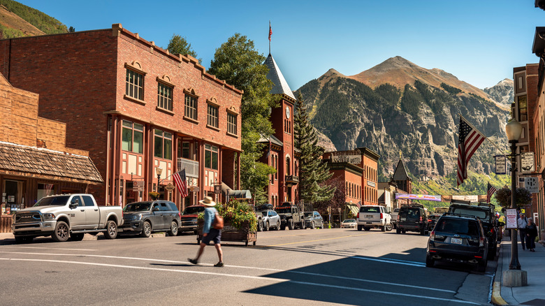 A pedestrian crosses a street in the summer in Telluride, Colorado, with mountains in the background