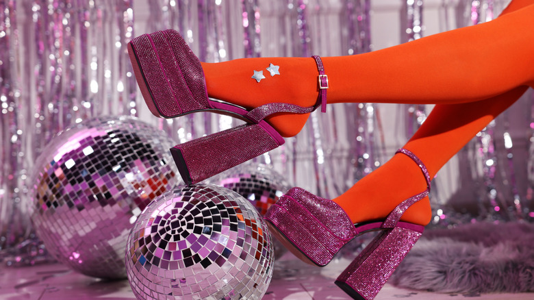 Woman in orange tights and pink high heeled shoes among disco balls indoors, closeup of shoes