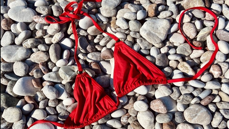 A bright red bikini top lying on a bed of pebbles