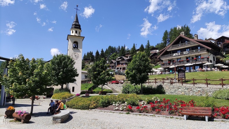 Chamois town center with a tall, white stone bell tower and a hillside covered with alpine-style buildings