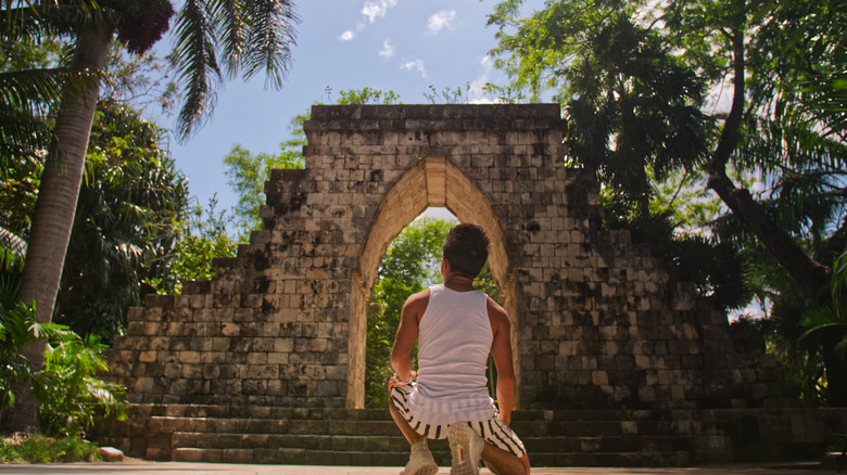 Back view of boy kneeling in front of Mayan structure