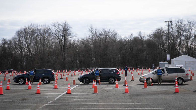 Line of cars entering a theme park parking lot with orange cones and attendants at each car window