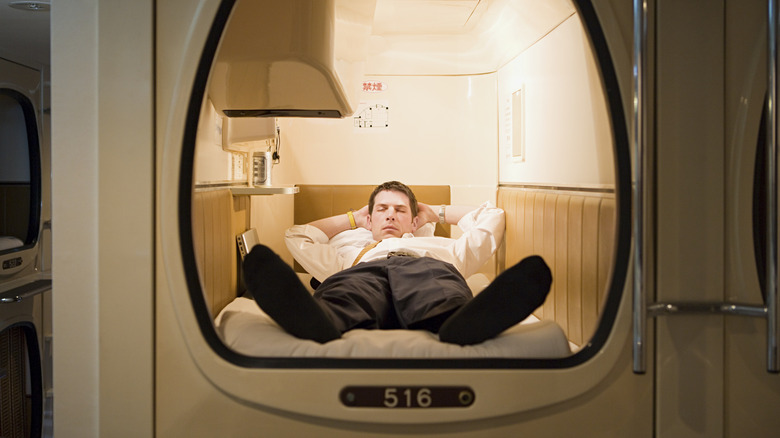 View of a Caucasian man resting in an extremely small capsule hotel room in Japan