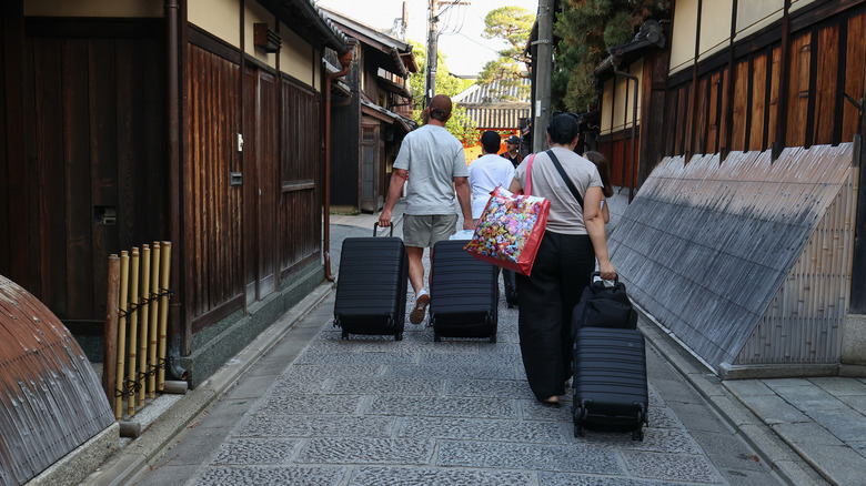 Back view of tourist family pulling large suitcases through a Japanese village amid traditional buildings