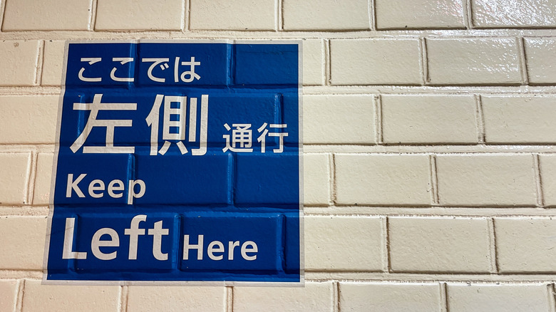 A bilingual English and Japanese sign saying "Keep Left Here" at a train station