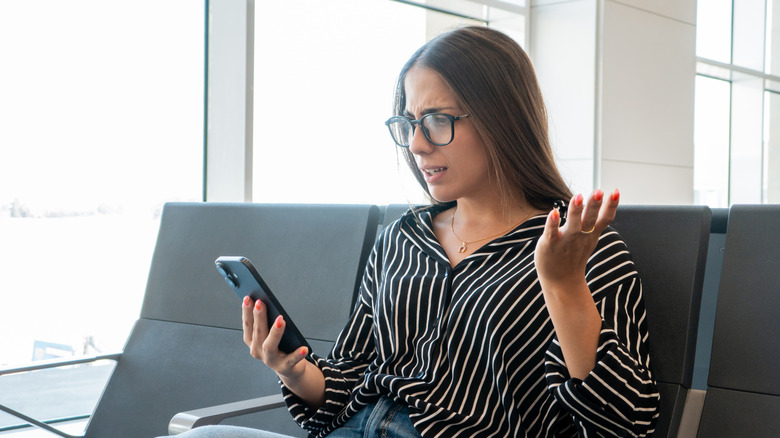 Frustrated young woman trying to resolve a problem on her cell phone while sitting at an airport gate
