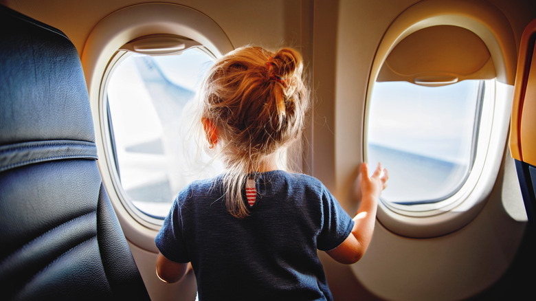 Back view of a little girl staring out the airplane window awaiting take-off