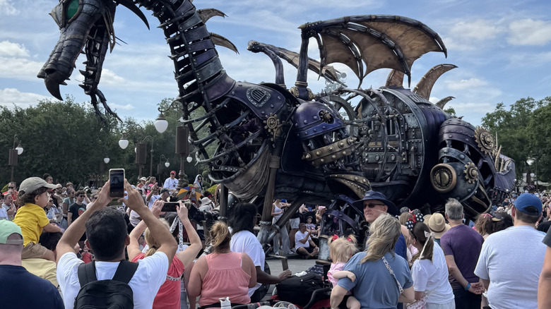 Throngs of people gather to take photos of a steampunk Maleficent dragon at Magic Kingdom on a sunny day