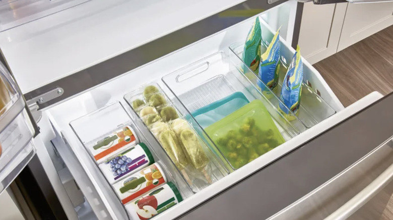 View of clear kitchen bin set filled with food items in a pull out freezer in a kitchen
