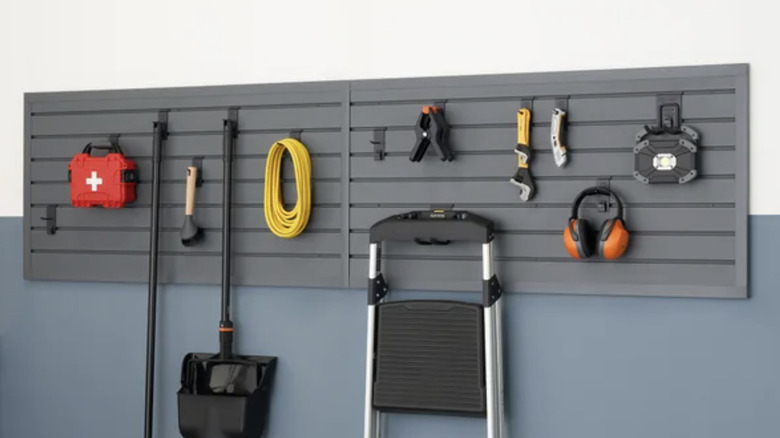 View of gray slatwall with first aid kid, power tools, brooms, a ladder and more