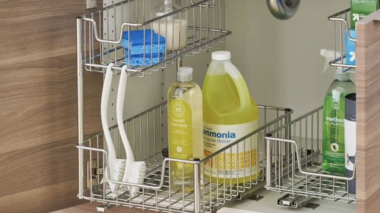 View of two sliding wire baskets filled with cleaning supplies under a sink