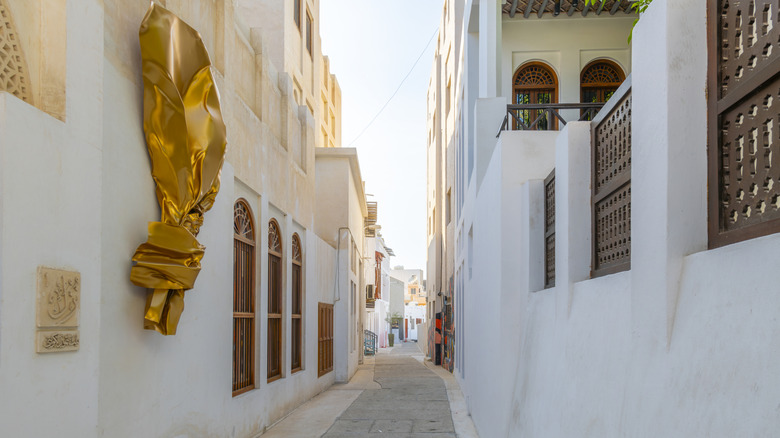 A narrow whitewashed alley in the Pearling Path old town district, with an ornate door and entrance to a traditional house in Muharraq, Bahrain in the Persian Gulf.