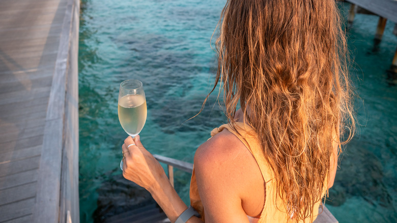 A woman standing on a pier with a glass of champagne in the Maldives