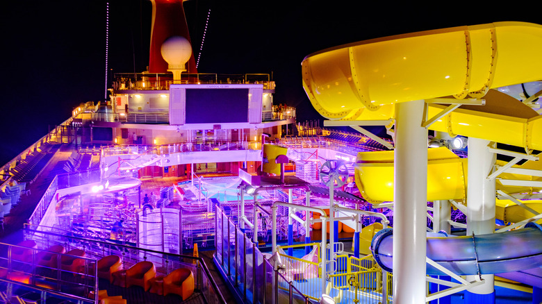 Nighttime view of Carnival Cruise Line ship deck with a yellow waterslide, purple-tinted lighting, and a huge screen for movies