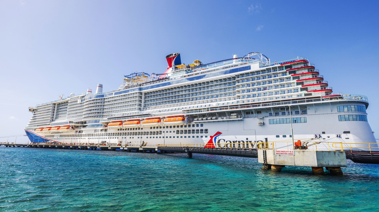 Side view of a Carnival Cruise Line ship docked in turquoise water with a bright blue sky