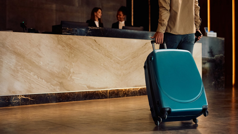 Close up of hotel guest with a suitcase arriving reception desk.