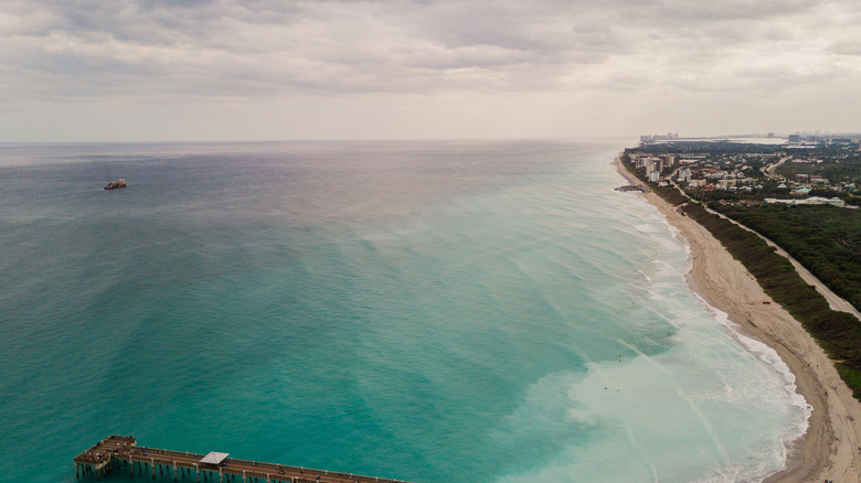 Aerial view of the empty Juno Beach seashore with bright turquoise water on a cloudy day