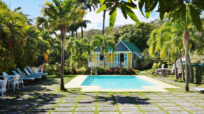 View of the yellow house, the pool, and lush tropical landscaping at Hermitage Nevis on a sunny day