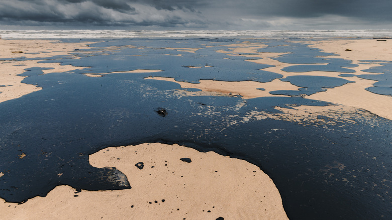 Close up of large oil spill on beach with stormy skies in the background