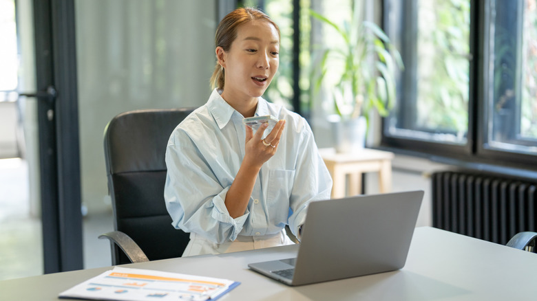 Woman front of a computer holding a cellphone in an office