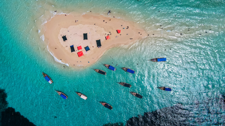 Aerial view of boats surrounding small sandy atoll