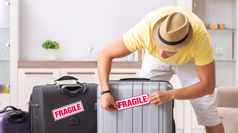 A man packing a suitcase with a fragile sticker on it