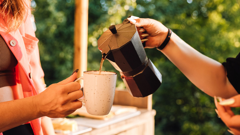 Hands pouring coffee from a moka pot outdoors