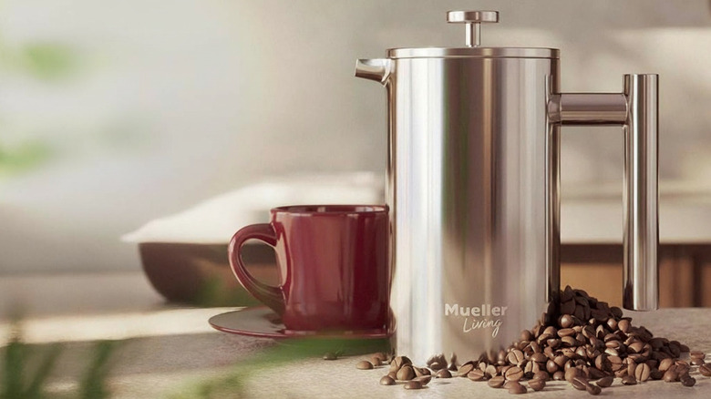 A MuellerLiving French Press next to a freshly poured cup with coffee beans by its side.