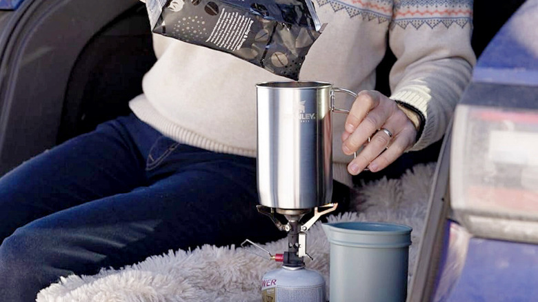 Adding coffee to the STANLEY All-in-One Boil + Brew French Press in the back of a car.