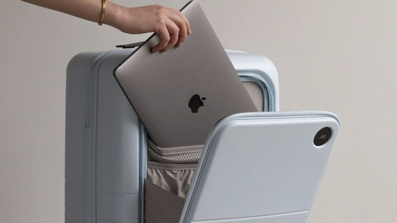 Close up of woman's hand placing an Apple laptop into the exterior sleeve on a light blue Monos suitcase