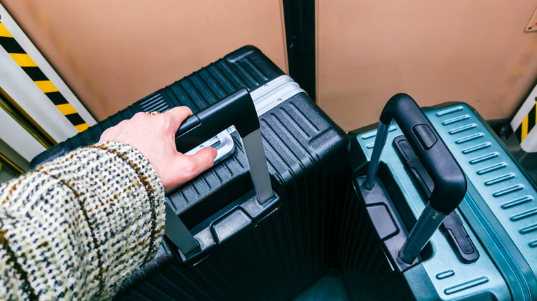 View of traveler holding black suitcase handle inside train next to teal luggage