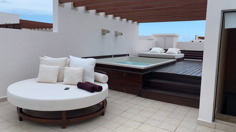 View of hot tub, white and teak resort furniture, and Pueblo-style architecture at Excellence Resort Playa Mejueres, Mexico