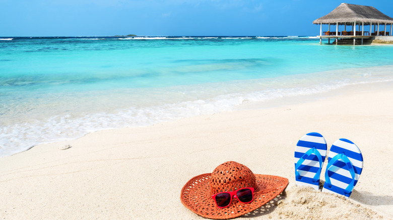 Sun hat with sunglasses and flip flops at tropical beach