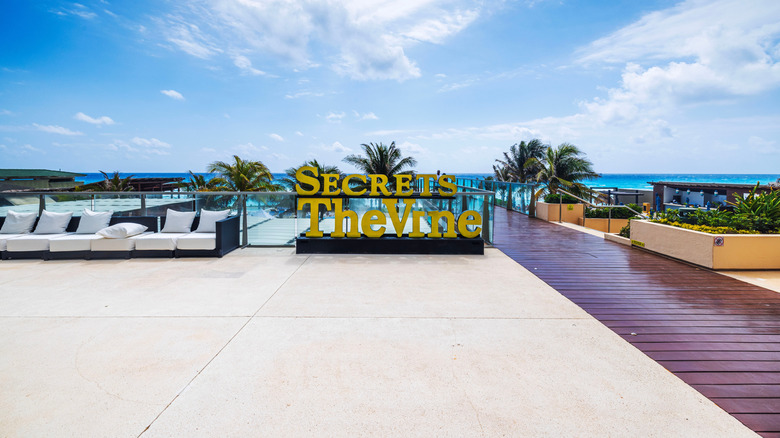 View of Secrets The Vine sign on deck at Mexican resort with modern design, wooden walkway and Caribbean sea view