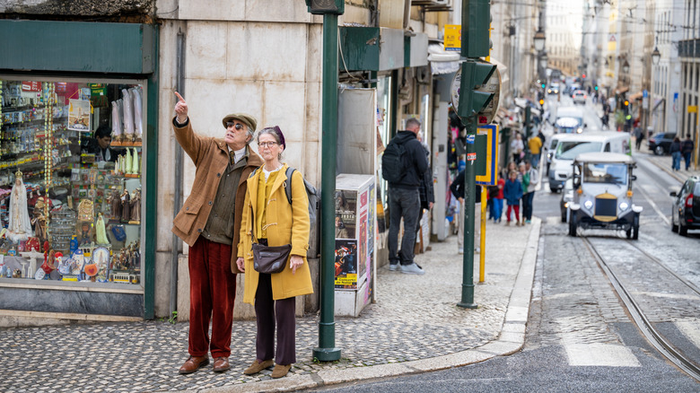 Elderly Caucasian couple standing at a street corner, man pointing