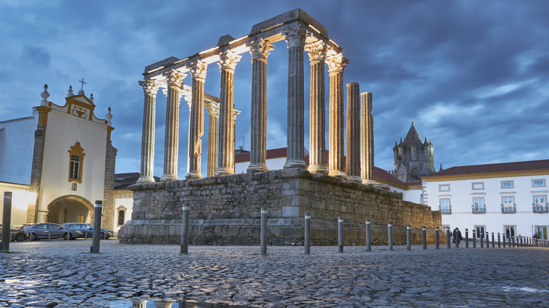 Corrinthian columns in the middle of cobble-stoned square, overcast skies, church on one side