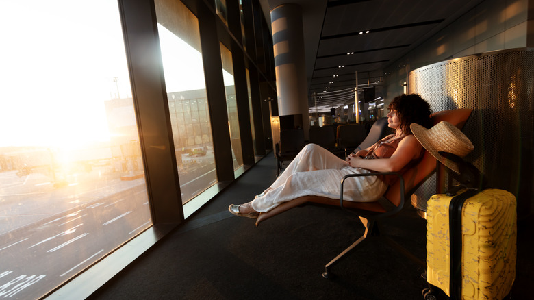 Woman looking out of the window at a runway as she waits at the airport