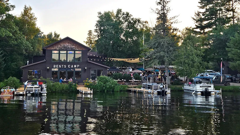 The exterior of Bent's Camp, Land O' Lakes, Wisconsin, viewed from the water with boats moored at the lakeshore