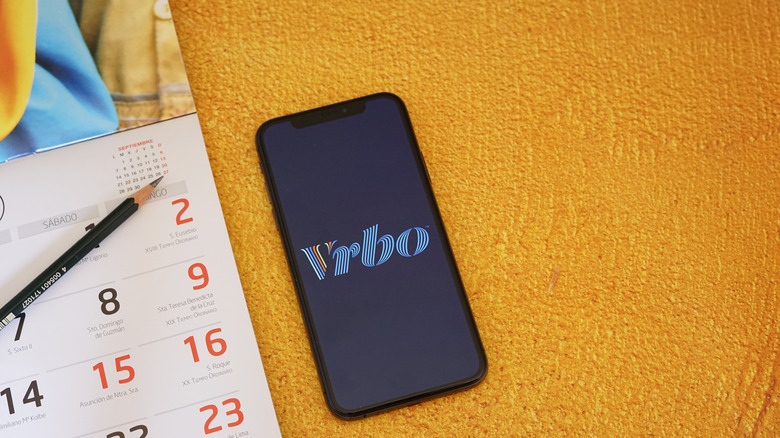 Phone with the Vrbo app displayed next to a calendar and pencil