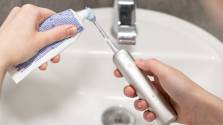 Close-up of hands putting toothpaste on a flight-safe electric toothbrush over a hotel sink