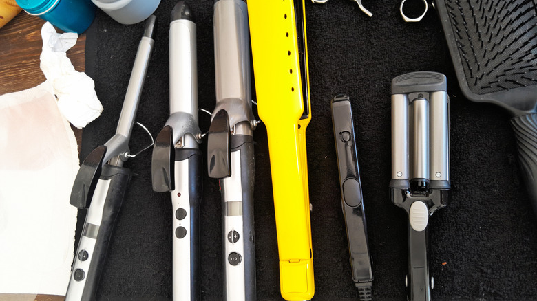 Hair tools, including curling irons and a yellow straightener, on a black mat on a wood table