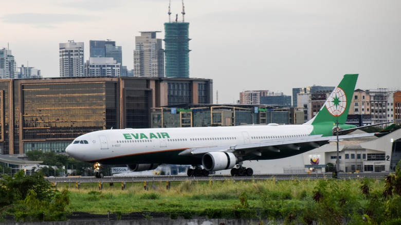 Green and white EVA Air plane on the runway in Manila, Philippines with skyscrapers in the background