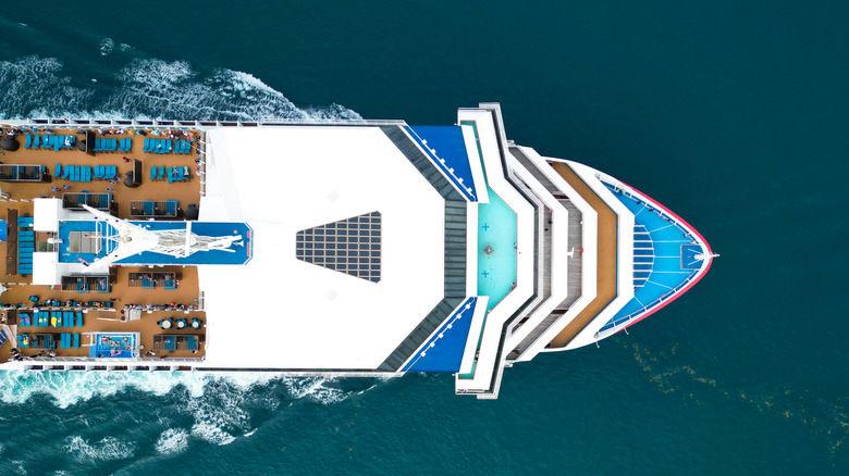 Aerial view of the bow of a cruise ship with the pool deck and blue loungers visible with a deep blue ocean beneath the ship